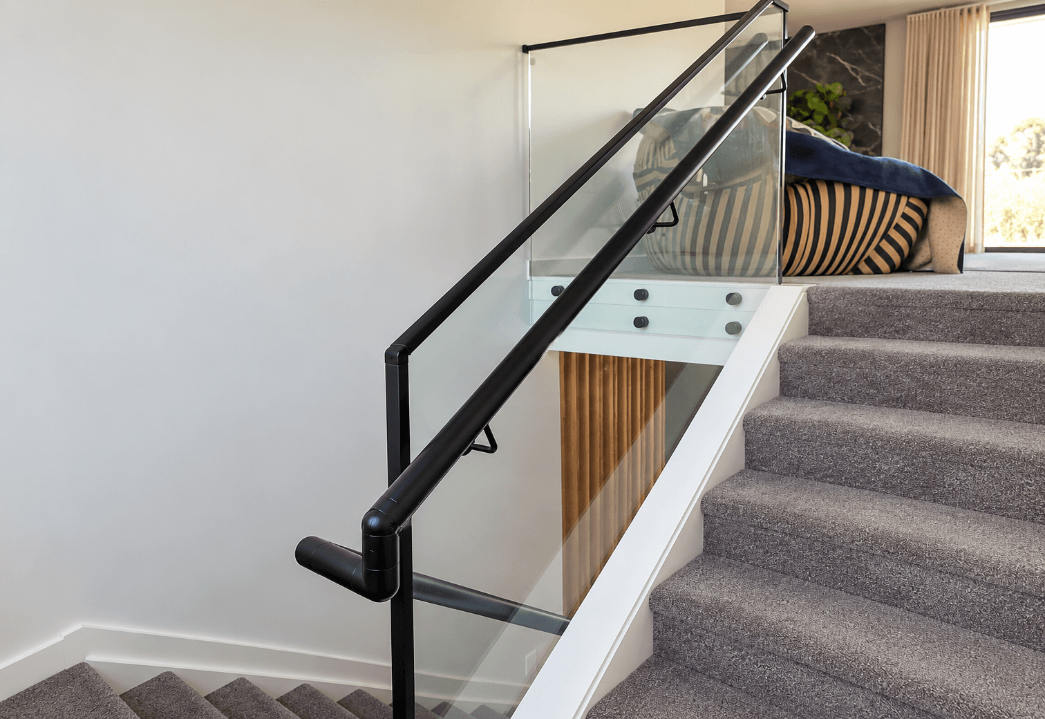 Black handrail with a black-framed glass balustrade beside carpeted stairs