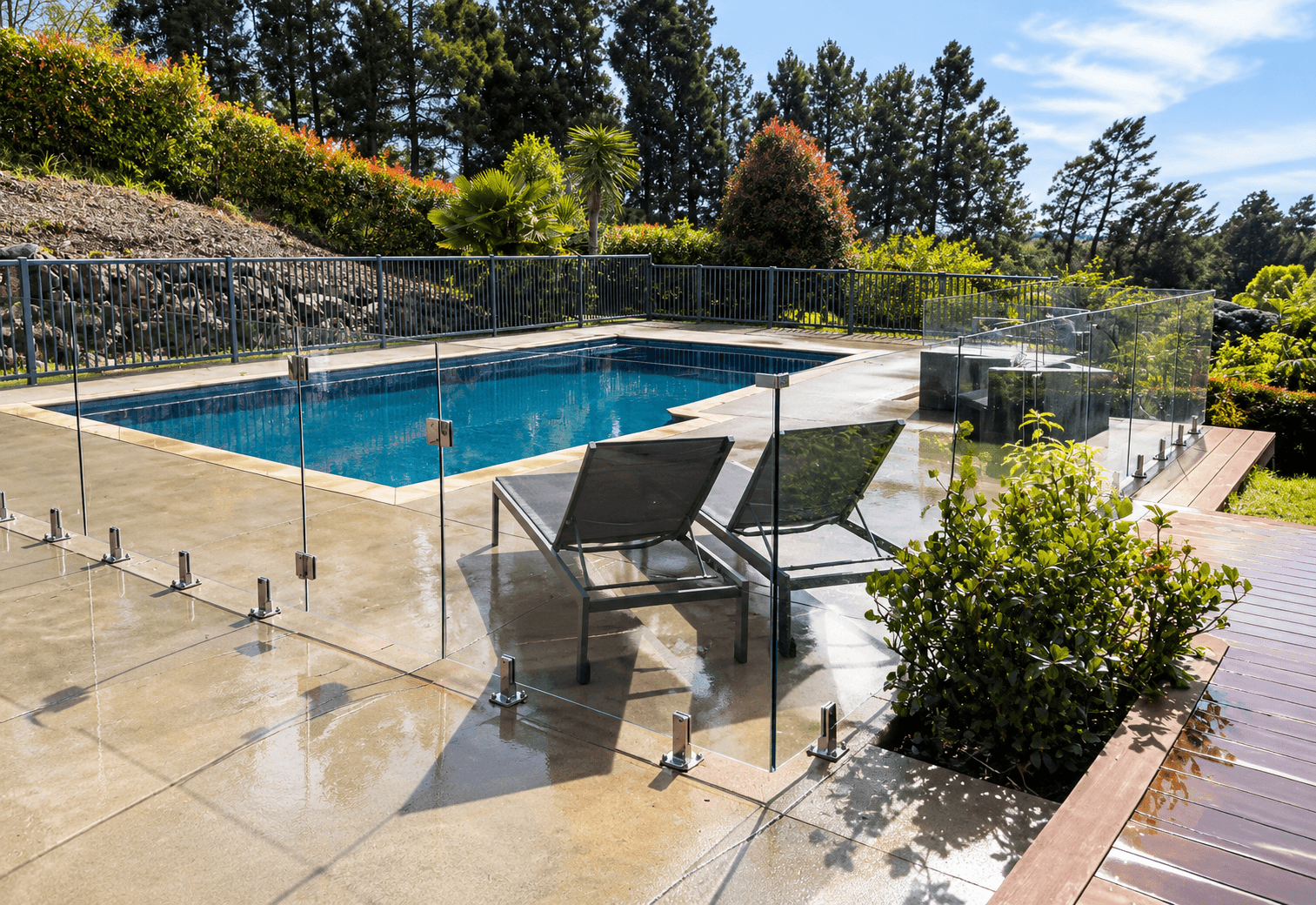 Glass pool fence with silver spigots around a landscaped pool