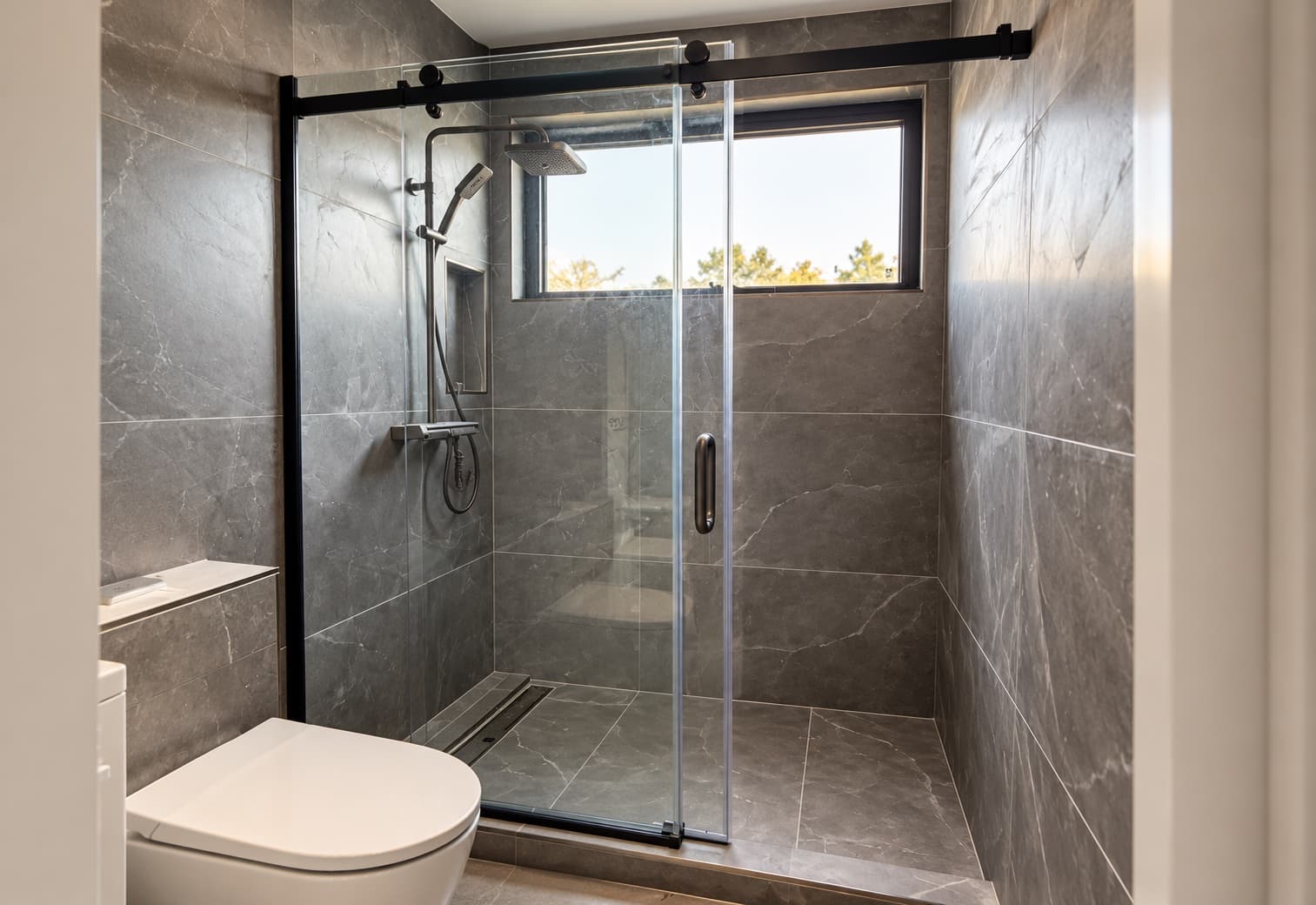 Walk-in glass shower with dark marble-look tiles